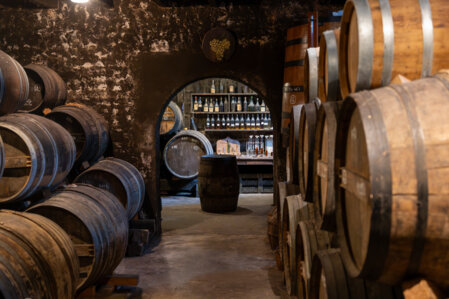 Caveau dans lequel se trouvent de nombreux tonneaux et plusieurs bouteilles de vin derrière un bar
