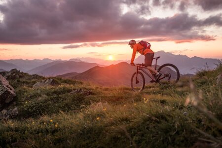 Un guide VTT en pleine sortie dans les montagnes face à un coucher de soleil