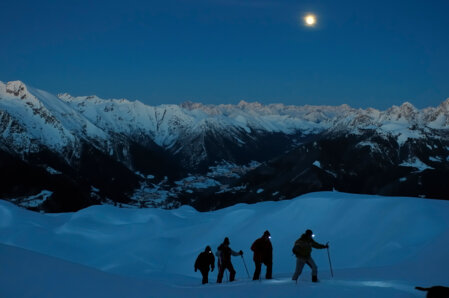 Un groupe marche dans un paysage enneigé, sous la lueur de la lune et des lompes frontales