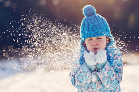 Une petite fille souffle dans ses mains remplies de neige