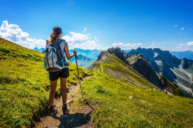 Une randonneuse marche sur un sentier et profite d'un beau panorama sur les montagnes alpines